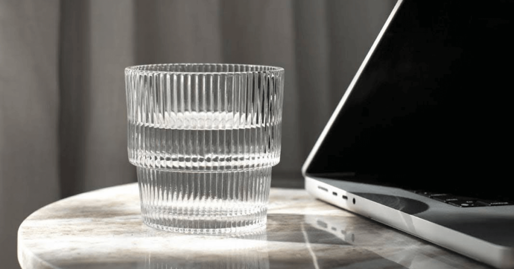 glass on a desk next to a laptop
