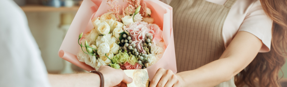 Florist handing a wrapped flower bouquet to a customer in a flower shop.