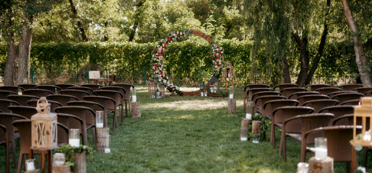 Outdoor wedding ceremony setup at a wedding venue featuring an aisle, wooden chairs, and floral arbor